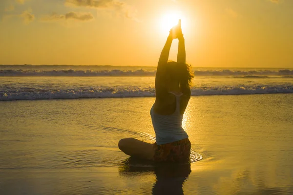 Silueta de joven en forma y atractiva mujer deportiva en playa puesta de sol yoga práctica entrenamiento sentado en sol húmedo frente al mar en meditación relajación — Foto de Stock