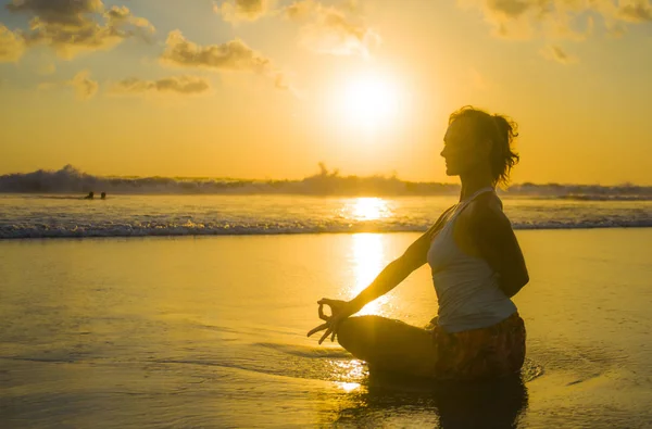 Silueta de joven en forma y atractiva mujer deportiva en playa puesta de sol yoga práctica entrenamiento sentado en sol húmedo frente al mar en meditación relajación — Foto de Stock