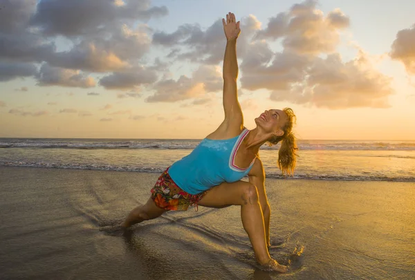 Mujer joven en forma y atractivo deporte en playa puesta del sol yoga práctica de entrenamiento en sol húmedo en frente del mar en la meditación y el ejercicio de relajación — Foto de Stock