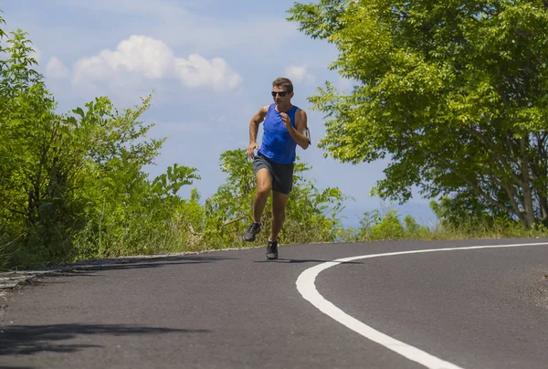 Młoda atrakcyjna sportu runner człowiek szkolenia w asfaltową drogą systemem treningu, słoneczny letni poranek otoczony przez drzewa i roślinności — Zdjęcie stockowe