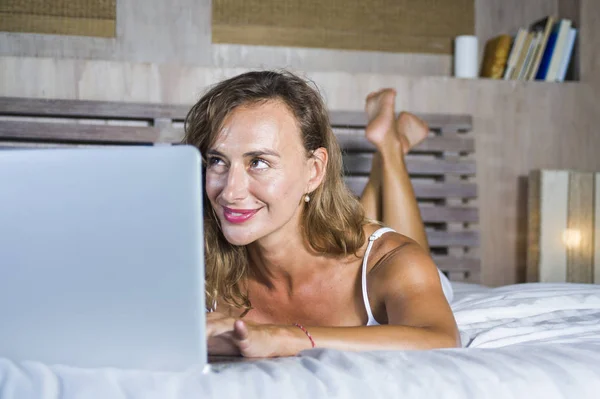 Fiatal vonzó és szép boldog kaukázusi nő feküdt az ágyban, a 30-as otthon, interneten keresztül a számítógép laptop mosolygós, nyugodt és vidám dolgozik — Stock Fotó