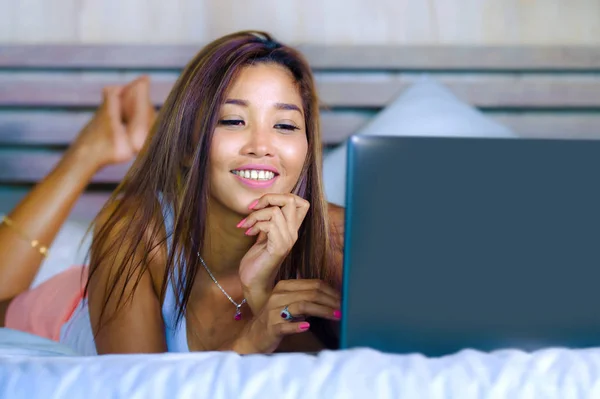 Jonge mooie en gelukkig Aziatische Hispanic gemengd ras vrouw die lacht op thuis slaapkamer liggend op bed met behulp van internet op computer laptop ontspannen en chill — Stockfoto