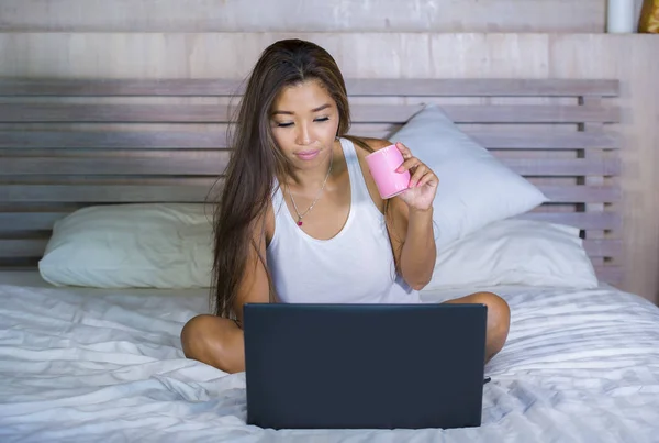 Jeune attrayant et heureux asiatique hispanique ethnicité mixte femme au lit en utilisant ordinateur portable étudier ou profiter de l'Internet détendu boire du café — Photo