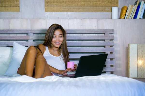 Jonge aantrekkelijke en gelukkig Aziatische hispanic etniciteit gemengd vrouw in bed met laptopcomputer studeren of genieten van de ontspannen koffie drinken internet — Stockfoto