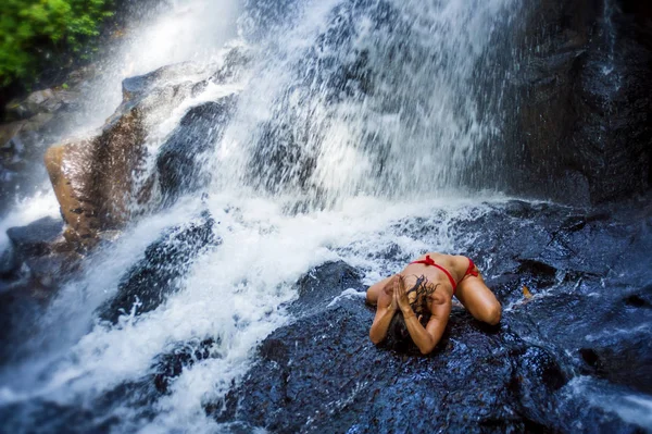 Jovem mulher feliz e atraente fazendo exercício de ioga posando sob bela cachoeira tropical ficando molhado sorrindo feliz em meditaton — Fotografia de Stock