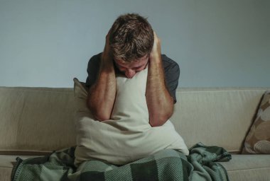 Genç üzgün ve umutsuz adam evde kapsayan yüz eller ve acı depresyon ağlıyor yastık ile kanepe oturma kanepe oturma ve duygu sefil üzüntü ve yaşam tarzı kavram stres