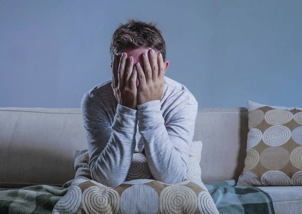 年轻的悲伤和绝望的男人在家里坐在沙发沙发上抱着头用手承受抑郁和压力担心问题独自哭泣悲伤和生活方式的概念 — 图库照片