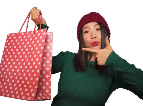 Joven hermosa y feliz mujer coreana asiática en fresco sombrero de invierno celebración bolsa de compras emocionada compra regalo de Navidad sonriendo en concepto de belleza de moda aislado —  Fotos de Stock