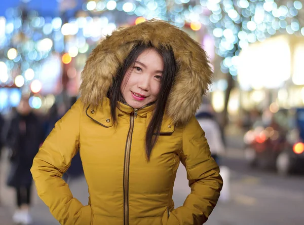 Ao ar livre retrato de inverno de jovem bonita e feliz mulher coreana asiática em casaco capuz quente desfrutando de férias de Natal sorrindo brincalhão e despreocupado em uma rua decorada — Fotografia de Stock