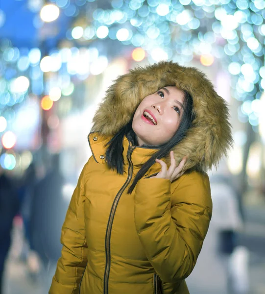 Al aire libre retrato de invierno de joven hermosa y feliz mujer coreana asiática en chaqueta de capucha caliente disfrutando de vacaciones de Navidad sonriente juguetón y despreocupado en una calle decorada — Foto de Stock