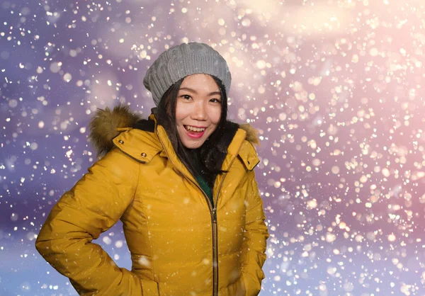 Jovem bela e feliz asiática estudante chinesa mulher no chapéu de inverno e casaco capuz quente desfrutando de neve de Natal sorrindo alegre e despreocupado no fundo isolado — Fotografia de Stock