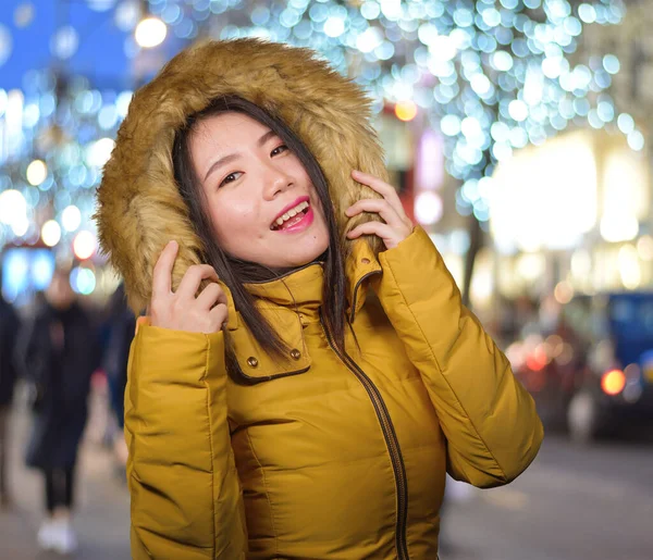 Al aire libre retrato de invierno de joven hermosa y feliz mujer coreana asiática en chaqueta de capucha caliente disfrutando de vacaciones de Navidad sonriente juguetón y despreocupado en una calle decorada — Foto de Stock