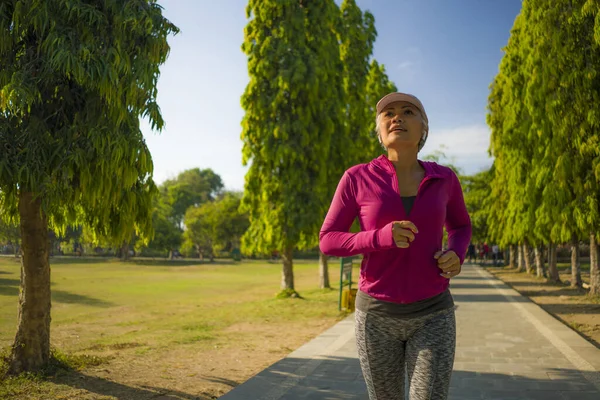 Atraente mulher de meia-idade correndo feliz no parque da cidade. bela e desportiva senhora no seu 40s exercício fazendo jogging treino em uma manhã ensolarada desfrutando — Fotografia de Stock