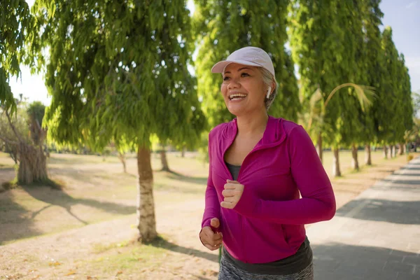 Şehir parkında mutlu koşan orta yaşlı çekici bir kadın. 40 'larında güzel ve sportif bir bayan güneşli bir sabahta egzersiz yapıyor ve eğleniyor. — Stok fotoğraf