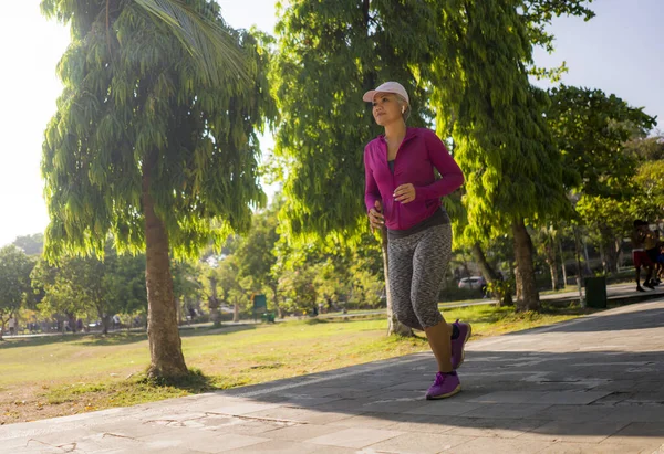 Attraktive Frau mittleren Alters läuft glücklich durch den Stadtpark. schöne und sportliche Dame um die 40 beim Jogging-Training an einem sonnigen Morgen — Stockfoto