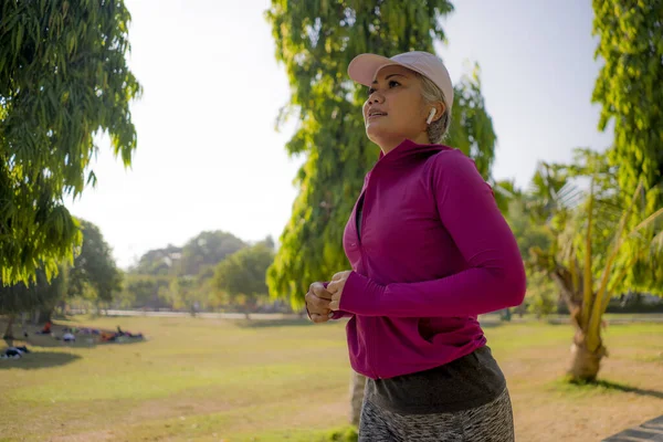 Atraente mulher de meia-idade correndo feliz no parque da cidade. bela e desportiva senhora no seu 40s exercício fazendo jogging treino em uma manhã ensolarada desfrutando — Fotografia de Stock