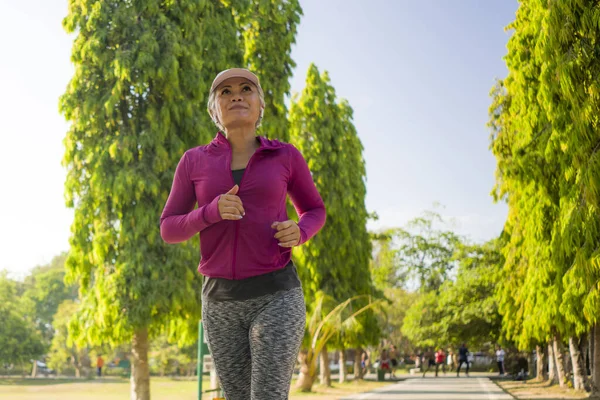 Attraente donna di mezza età in esecuzione felice al parco della città. bella e sportiva signora sui suoi 40s esercizio facendo jogging allenamento in una mattina di sole godendo — Foto Stock