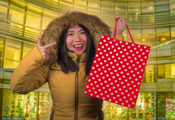 행복하고 아름다운 동양인 여성 이 쇼핑백을 들고 크리스마스 선물을 사고 있습니다 따뜻 한 겨울 후드를 입고 기뻐하며 — 스톡 사진