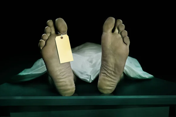 Male human body lying dead at morgue with blank identity label and covered with sheet . Close-up foot of man cadaver with identification toe tag in death concept — Stock Photo, Image