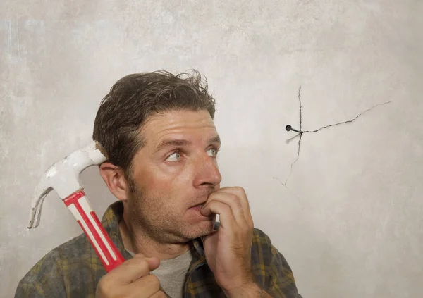 Retrato engraçado de homem segurando martelo depois de dirigir um prego para pendurar uma moldura, mas fazendo uma bagunça rachando a parede como um cara desastre DIY e tarefa de reparo doméstico bagunçado — Fotografia de Stock