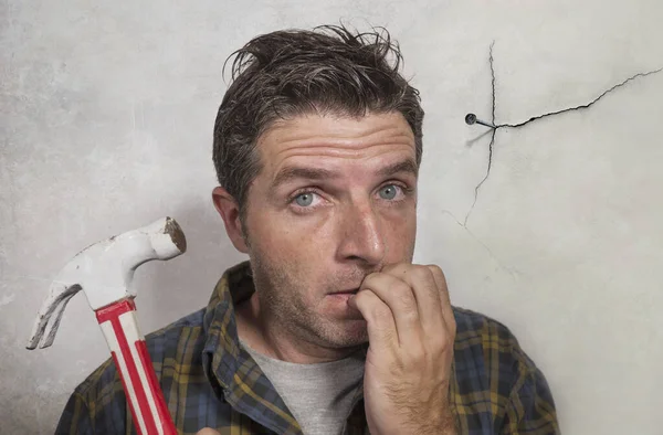 Mann mit Hammer, der einen Nagel für das Aufhängen eines Rahmens schlägt, aber lustige Gesichter für das Chaos macht, das die Wand als Katastrophen-Dieb und chaotische häusliche Reparaturaufgabe zerbricht — Stockfoto