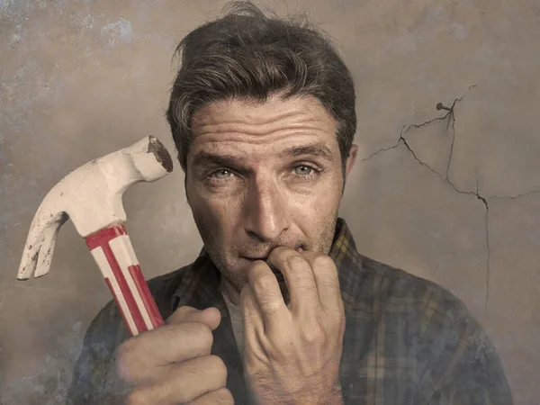 Hombre sosteniendo un martillo clavando un clavo para colgar un marco, pero haciendo caras divertidas para el lío que agrieta la pared como un tipo de DIY desastre y tarea de reparación doméstica desordenada — Foto de Stock