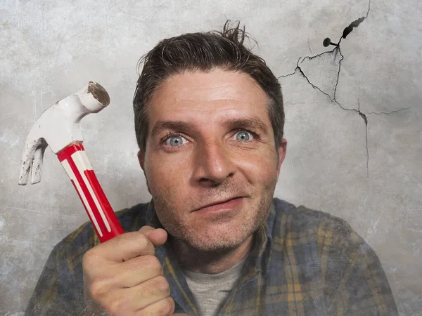 man holding hammer driving a nail for hanging a frame but making funny faces for the  mess cracking the wall as a disaster DIY guy and messy domestic repair task