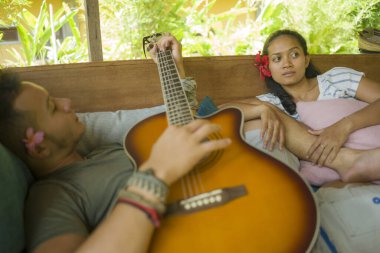 Genç, güzel ve mutlu, melez bir çift. Hipster tarzında dışarıda gitar çalıyor. Huzur bahçesinde rahatça gitar çalıyor.
