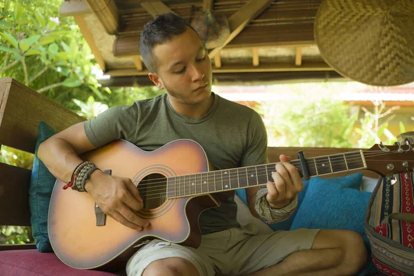 Jovem bonito e feliz misto etnia homem em estilo hipster arrepiante ao ar livre tocando guitarra relaxado no tranquilo jardim tropical desfrutando de férias retiro — Fotografia de Stock