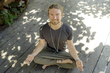 Yenilikçi adam yoga yapıyor. Genç, çekici ve mutlu atletik bir adam, Lotus pozu vermiş, meditasyon egzersizi yapıyor, rahatlamış ve zen gibi gülümsüyor.