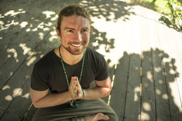 hipster guy practicing yoga . young attractive and happy athletic man sitting on resort bed in lotus pose doing meditation exercise smiling relaxed and zen like in harmony