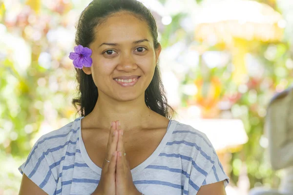 Jovem bela e feliz mulher indonésia asiática com flor de orelha estilo balinês em mãos Namaste posar sorrindo no estúdio de ioga relaxado e zen como em harmonia — Fotografia de Stock