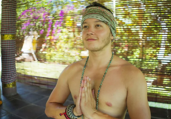 Jovem meditação hipster bonito sentado em posição de lótus - Attractive atlético e feliz homem praticando ioga relaxamento exercício vestindo faixa de cabelo e colar de contas mala — Fotografia de Stock