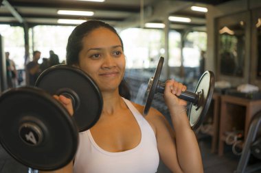 Genç, çekici ve mutlu, Endonezyalı, spor salonundaki halterleri kaldıran Endonezyalı kadın spor ve vücut geliştirme konseptinde terli ve neşeli.