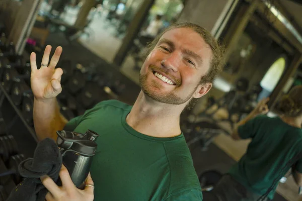 Naturlig fitness livsstil porträtt av ung glad och attraktiv man hålla flaska vatten träning på gym leende glad efter hård bodybuilding träning ger ok tecken — Stockfoto