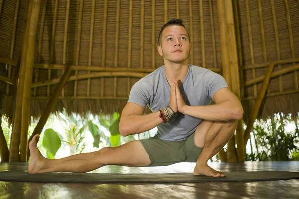 young attractive and happy man doing yoga drill and stretching exercise smiling relaxed in harmony at beautiful Asian bamboo hut enjoying nature in body mind balance