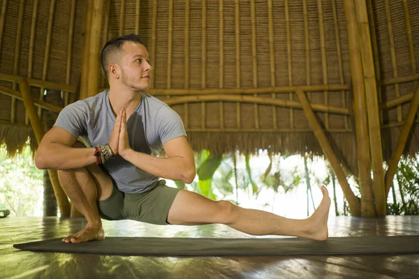 Junger attraktiver und glücklicher Mann, der Yoga-Übungen und Stretchübungen macht, lächelt entspannt in Harmonie in einer wunderschönen asiatischen Bambushütte und genießt die Natur im körperlichen Gleichgewicht — Stockfoto