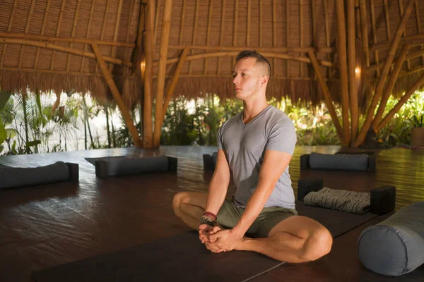 Junger attraktiver und glücklicher Mann macht Yoga sitzend in Lotusposition und meditiert entspannt in Harmonie in einer wunderschönen asiatischen Bambushütte und genießt die Natur im körperlichen und geistigen Gleichgewicht — Stockfoto