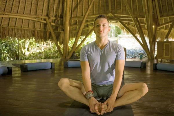 young attractive and happy man doing yoga sitting in lotus position meditating relaxed in harmony at beautiful Asian bamboo hut enjoying nature in body and  mind balance