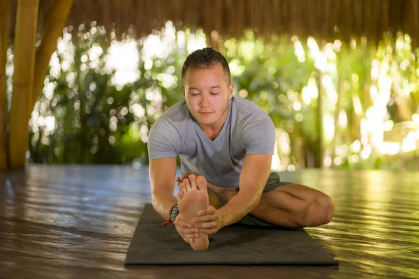 Attraktiver und glücklicher Mann, der Yoga-Übungen und Stretchübungen macht, lächelt entspannt in Harmonie in einer wunderschönen asiatischen Bambushütte und genießt die Natur im körperlichen und geistigen Gleichgewicht — Stockfoto