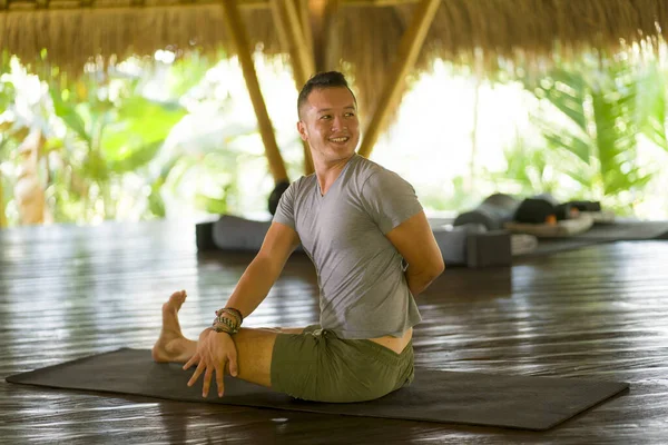 Attraktiver und glücklicher Mann, der Yoga-Übungen und Stretchübungen macht, lächelt entspannt in Harmonie in einer wunderschönen asiatischen Bambushütte und genießt die Natur im körperlichen und geistigen Gleichgewicht — Stockfoto