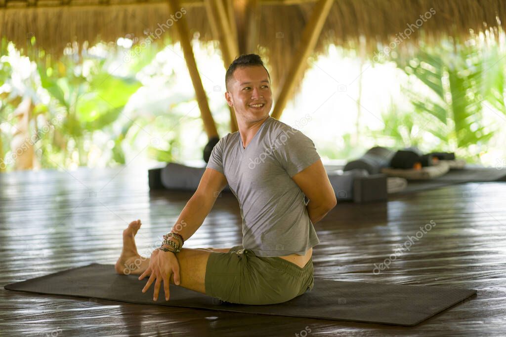 attractive and happy man doing yoga drill and stretching exercise smiling relaxed in harmony at beautiful Asian bamboo hut enjoying nature in body and mind balance