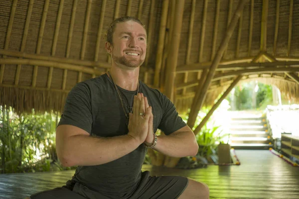 Jovem atraente e feliz homem no estilo hipster yogi fazendo ioga broca na bela cabana de bambu asiático em namaste mãos posição apreciando a natureza no corpo mente equilíbrio — Fotografia de Stock