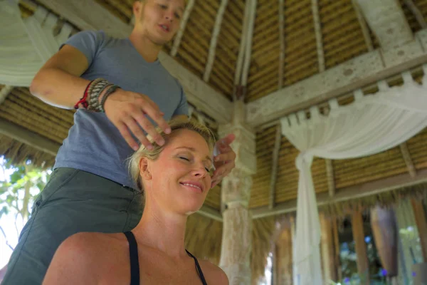 Primer plano masajista manos y cara de joven hermosa y feliz turista americana teniendo masaje tradicional en el spa asiático al aire libre disfrutando de vacaciones retiro — Foto de Stock