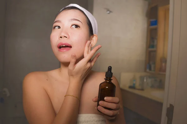 Potret gaya hidup alami wanita Cina Asia yang cantik dan bahagia mengenakan kosmetik serum anti penuaan di wajahnya di kamar mandi rumah tersenyum segar dalam perawatan kulit wajah — Stok Foto