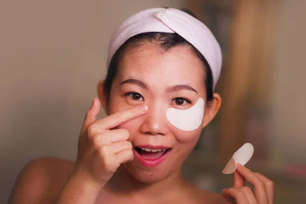 Muda cantik dan bahagia wanita Asia Jepang tersenyum ke kamar mandi cermin menerapkan hydrating eye patch di bawah mata kosmetik kecantikan dan perawatan kulit wajah — Stok Foto