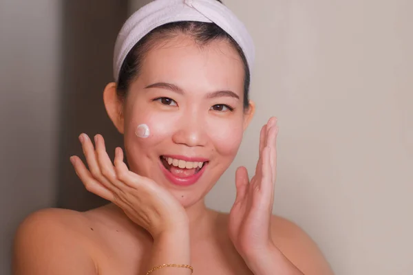 Portrait de style de vie domestique de jeune belle et heureuse femme asiatique coréenne appliquant la crème cosmétique faciale souriant gai au miroir de salle de bains dans les soins de la peau beauté — Photo