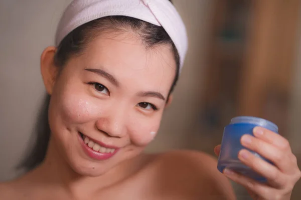 Домашній портрет молодої красивої і щасливої азіатської корейської жінки, яка застосовує косметичне крем "ясо, посміхаючись до туалетного дзеркала в догляді за шкірою. — стокове фото
