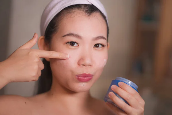 Estilo de vida doméstico retrato de joven hermosa y feliz mujer coreana asiática aplicación de crema cosmética facial sonriente juguetón al espejo de baño en el cuidado de la piel belleza — Foto de Stock