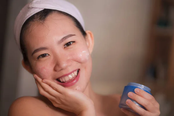 Güzel ve mutlu bir Asyalı kadının ev yapımı portresi. Yüzüne makyaj kremi sürüyor. Güzellik derisi bakımında banyo aynasına gülümsüyor. — Stok fotoğraf